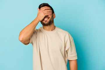 Young caucasian man isolated on blue background covers eyes with hands, smiles broadly waiting for a surprise.