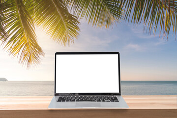 Empty screen laptop on a wooden table with coconut plam tree and sunset at tropical beach, Summer vacation concept