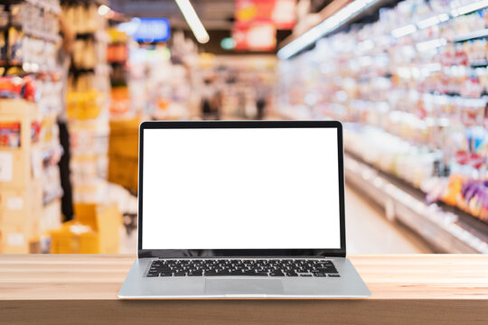 Empty screen laptop on a wooden table with abstract blurred image of supermarket store at the mall