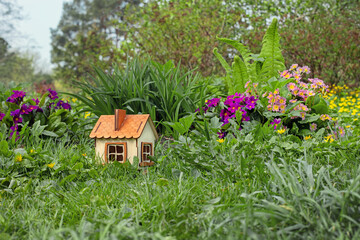 Naklejka na ściany i meble small wooden house in the garden, landscape design, blooming flowers and plants, green grass on an alpine slide, the concept of a happy family in a cozy home