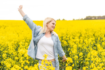 Fototapeta premium Portrait of attractive woman on blooming rapeseed field with sunset light. Yellow flowers and happy woman