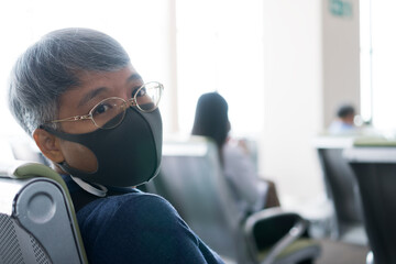 Asian COVID-19 protection situation in New Normal wear medical face mask protection virus corona pandemic outbreak for traveling, using Smartphone searching check-in flight timetable airport terminal