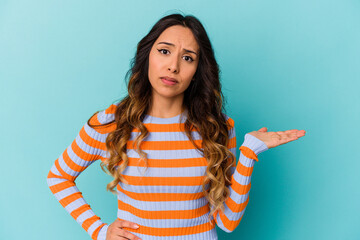 Young mexican woman isolated on blue background doubting and shrugging shoulders in questioning...