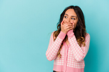 Young mexican woman isolated on blue background thoughtful looking to a copy space covering mouth with hand.