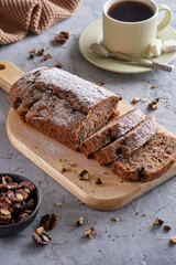 Delicious and flavorful banana cake with nuts and chocolate on a wooden board with a cup of coffee on a gray background
