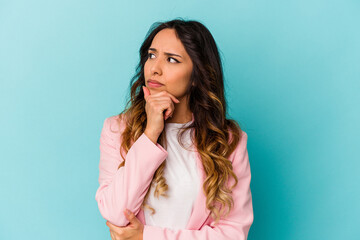 Young mexican woman isolated on blue background thinking and looking up, being reflective, contemplating, having a fantasy.