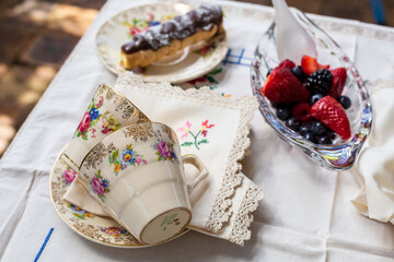 Outdoor afternoon tea setting with chocolate eclair and bowl strawberries and blueberries