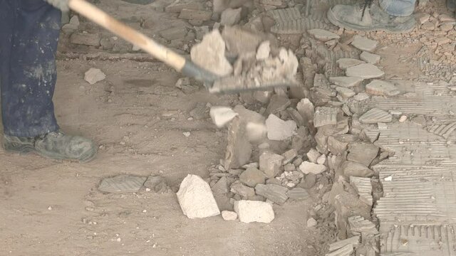 The builder takes apart the construction waste with a shovel. Builders are breaking down an old concrete floor.
