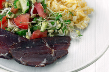 Closeup plate with complete diet meal. Slice of smoked meat, vegetable salad with microgreens, sprouts of cereals and broccoli, tomatoes, cucumbers, rice with eggs. Healthy energetic food. Copy space.