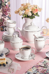 A photo of a set of white porcelain on a pink tablecloth in a composition with flowers