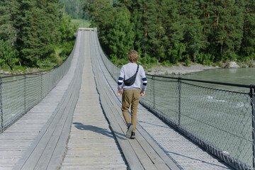 A young man running along an old wide mountain bridge over the river. Russian Siberian nature. Altai