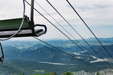 View of the cable way with chairlift, river and mountains from the top of the mountain in cloudy weather