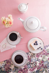 A photo of a set of white porcelain on a pink tablecloth in a composition with flowers