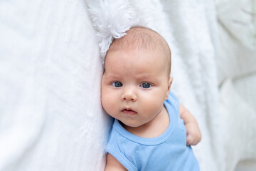 portrait of a cute baby boy three months old in a blue bodysuit on a white bed at home