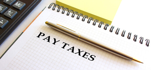 Notepad with text PAY TAXES, next to it lies a calculator. Business concept.