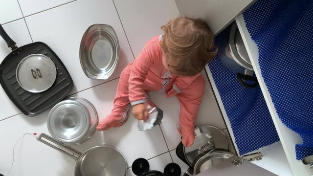 Baby toddler playing with kitchenware. Infant sitting on floor playing with coffee maker