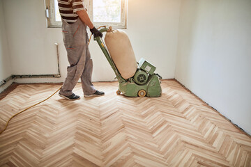 Repairman restoring parquet with a sanding machine.