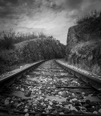 Train rail track into the distance leading between rocky hills. Black and white photo