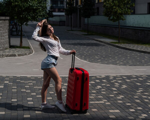 Beautiful caucasian brunette woman in a hat posing with a suitcase on a city street.