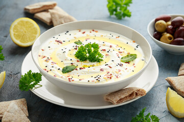 Labneh cream cheese dip with olive oil, salt, herbs served with olives, pita bread in white bowl