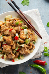 Stir fry chinese salt and pepper chicken with red, green chilli, onion, spring onion in white bowl.