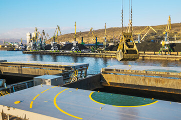 Huge amount of coal in the Murmansk commercial seaport. Loading of coal by buckets (grabs) of portal cranes into the holds of a dry cargo ship in the seaport