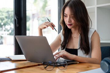 Beautiful young asian woman working on laptop computer while taking note at home office