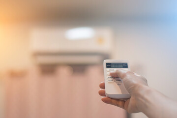 Close-up Of Young Woman Hand Operating Air Conditioner With Remote Control,Young woman switching on air conditioner at home,