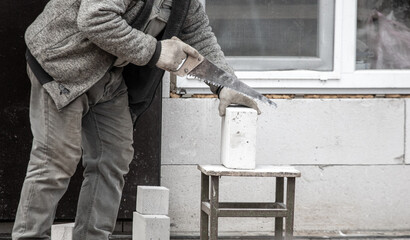 A worker cuts a brick with a saw.