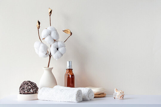 Bathroom Interior In Beige Pastel Tone. White Shelf In Bathroom With Towels, Soap, Perfume Bottle, Cotton Plant. Mockup With Space For Text. Minimal Composition.