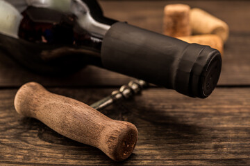 Fototapeta na wymiar Bottle of red wine with corks and corkscrew lying on an old wooden table. Close up view, focus on the bottle of red wine