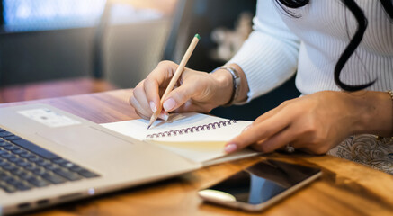 Closeup of hand asian businesswoman writing on notebook and using laptop to searching data for...