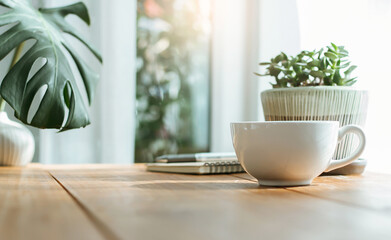 Closeup white cup of coffee with small trees and green leaf in vase on wooden table near bright...