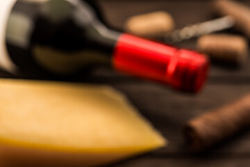 Bottle of red wine with a piece of parmesan and corkscrew with corks and cuban cigar lying on an old wooden table. Close up view, defocused image