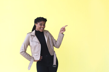 a beautiful and happy African-American woman points to a place for advertising, on a yellow background