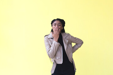 beautiful and happy African American woman blows a kiss on a yellow background