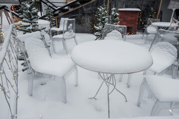 Tables and chairs in a cafe covered with snow outdoors.