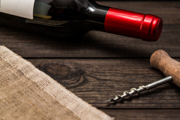 Bottle of red wine and piece of canvas with corkscrew lying on an old wooden table. Close up view, focus on the bottle of red wine