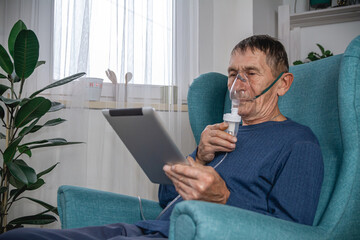 elderly senior sits in a armchair with an oxygen mask and tablet
