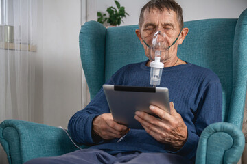 elderly senior sits in a armchair with an oxygen mask and tablet