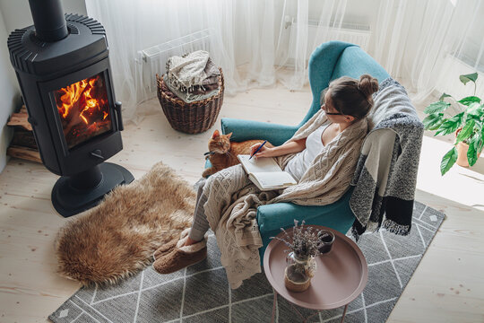 Young Woman  Write In A Notebook Sitting In A Armchair By The Fireplace