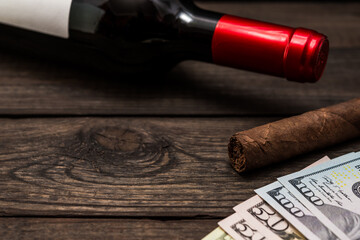 Bottle of red wine and cuban cigar with money on an old wooden table. Close up view, focus on the...
