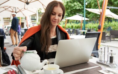 Woman drinking tea and working with laptop on cafe terrace