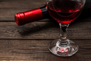 Bottle of red wine with a glass of red wine on an old wooden table. Close up view