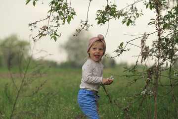 a girl in a pink headdress stands near a flowering tree and shows her tongue