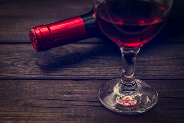 Bottle of red wine with a glass of red wine on an old wooden table. Close up view
