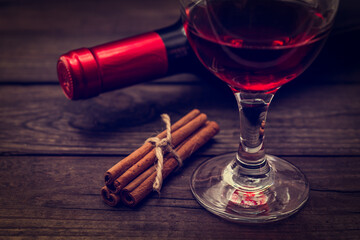 Bottle of red wine with a glass of red wine and  cinnamon sticks tied with jute rope on an old wooden table. Close up view, focus on the cinnamon sticks