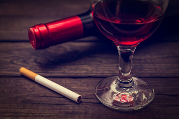 Bottle of red wine with a glass of red wine and cigarette on an old wooden table. Close up view, focus on the cigarette