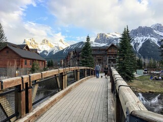 A couple going for an evening walk across a bridge surrounded by beautiful homes and mountains in a beautiful neighbourhood of Canmore, Alberta, Canada