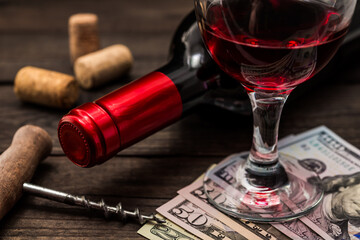 Bottle of red wine with a glass of red wine and money with corkscrew on an old wooden table. Close...